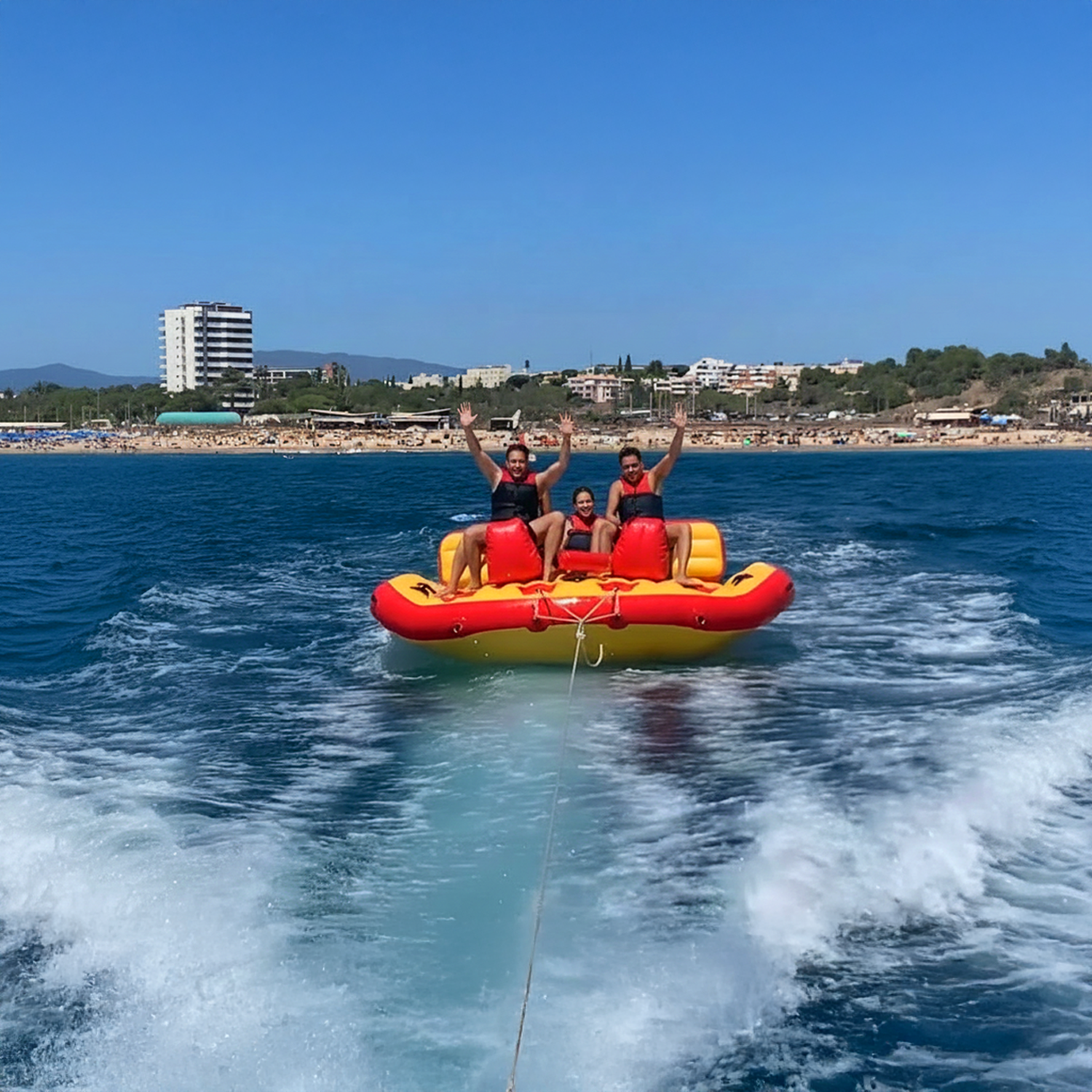 Group of people enjoying the Banana Slider - Inflatable Towable ride on the clear waters of Alvor, showcasing thrilling water fun.